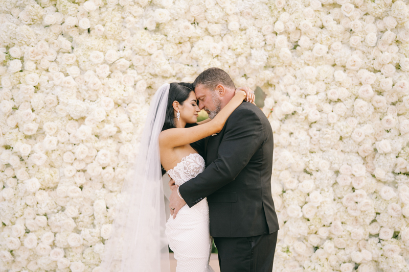 bride and groom portrait in front of white rose wall
