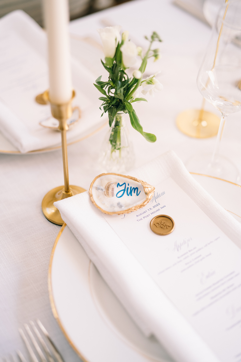 White plate with gold trim and white napkin under gold oyster with green flower