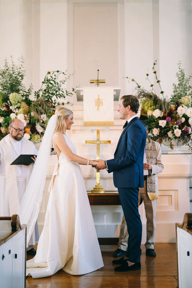 bride and groom at the altar holding hands and looking at each other smiling