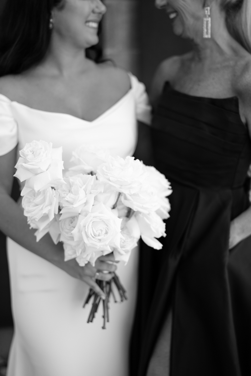 black and white photo of bride smiling with bridesmaid holding her flowers