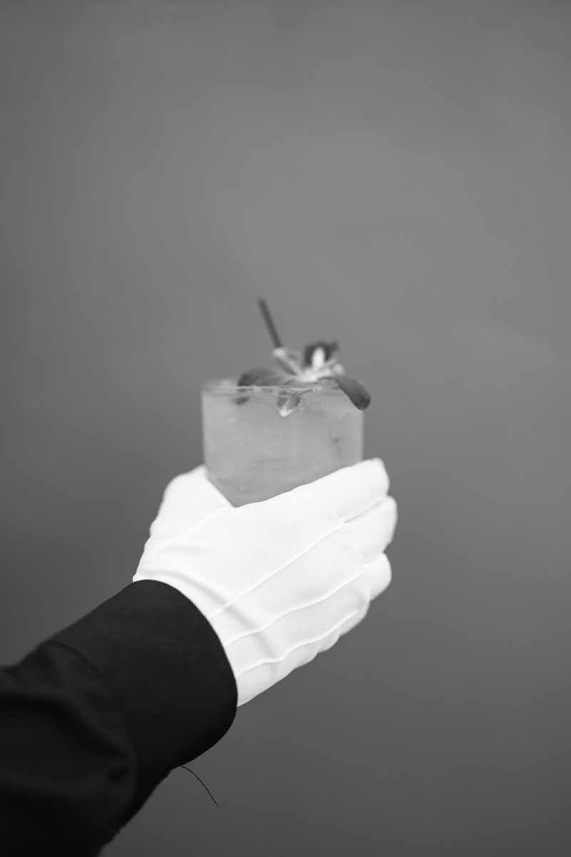 server in gloves holding a cocktail for wedding guests 