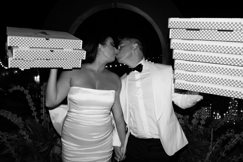 bride and groom kissing while holding pizza boxes