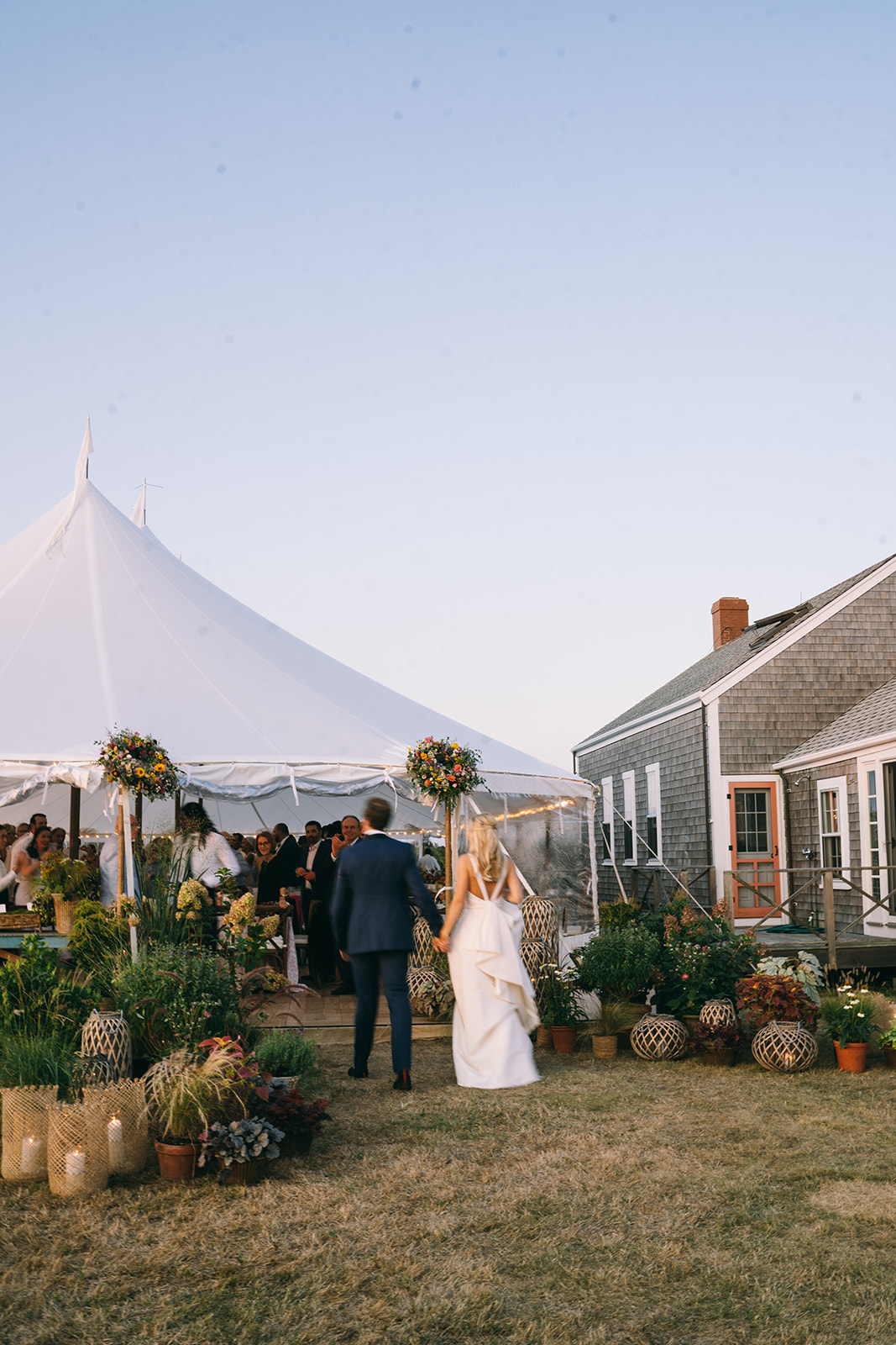 Bride and groom walking into the reception tent next to Nantucket cottage