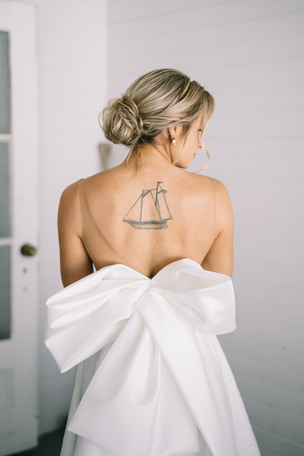 Back of bride's wedding dress with a huge bow with the bride looking to the side showing her back tattoo of a ship