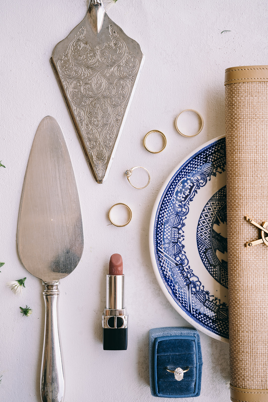 flat lay of antique cake cutters, wedding rings, a blue china plate and lipstick 