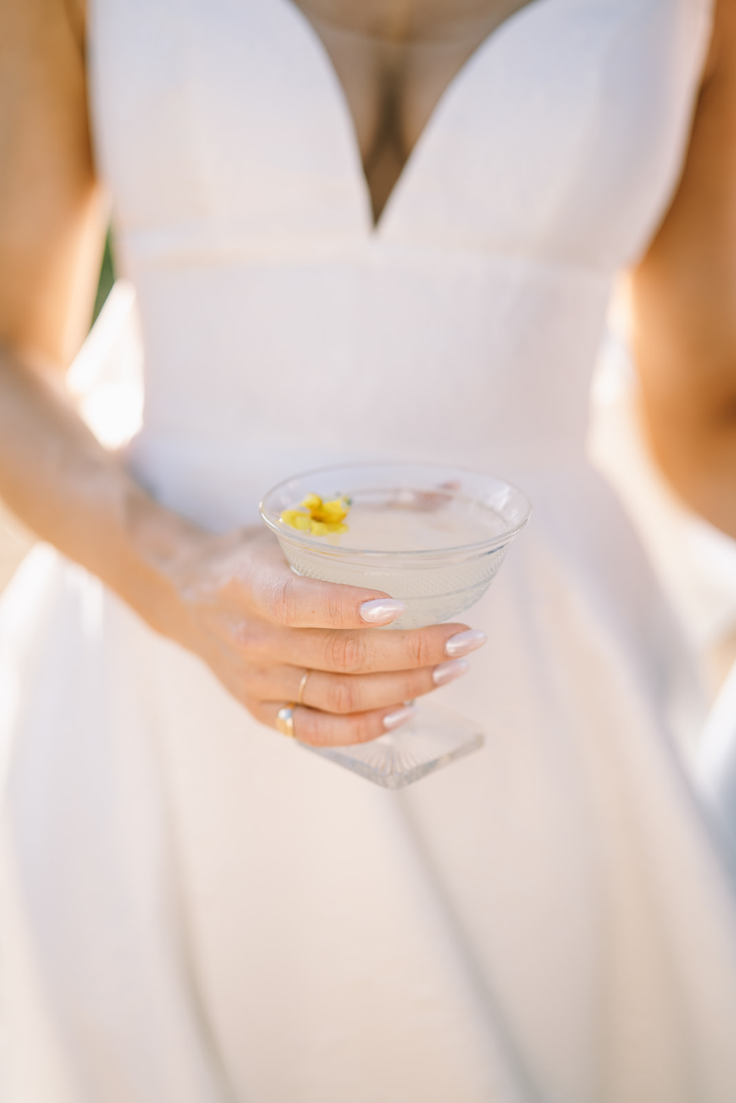 Close up of bride in wedding dress holding a cocktail with a yellow flower in it 