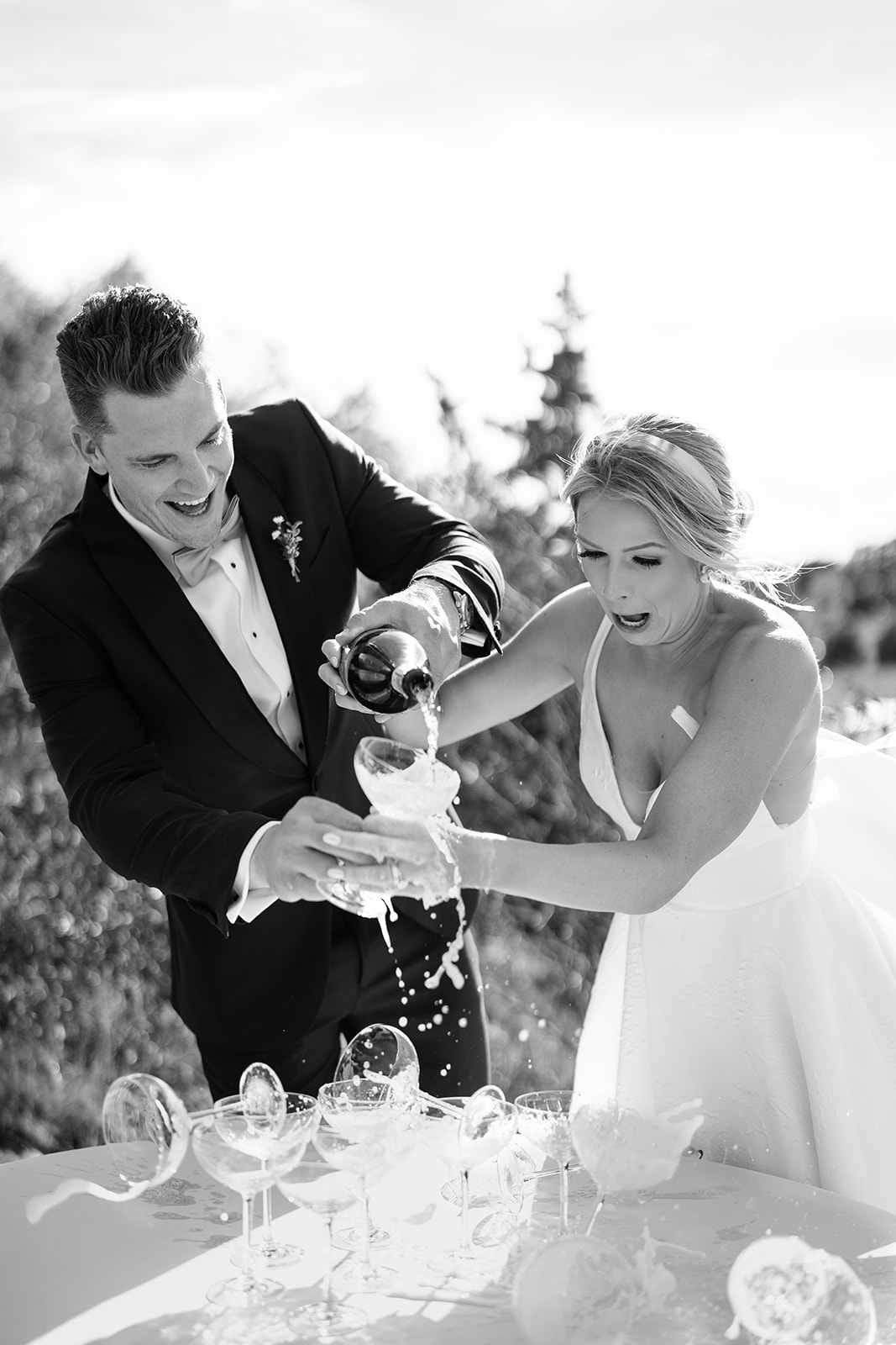 Bride and groom pouring champage into champagne tower that is simultaneously falling over with the bride and groom laughing 