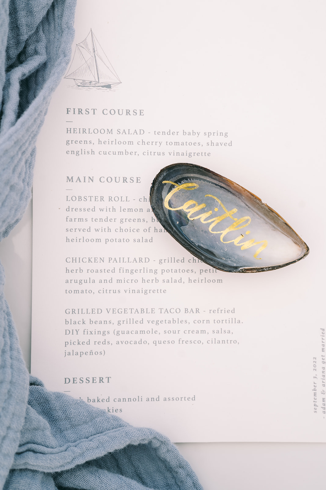 Close up of wedding menu with blue napkin with an oyster with the name 'Caitlin' on it