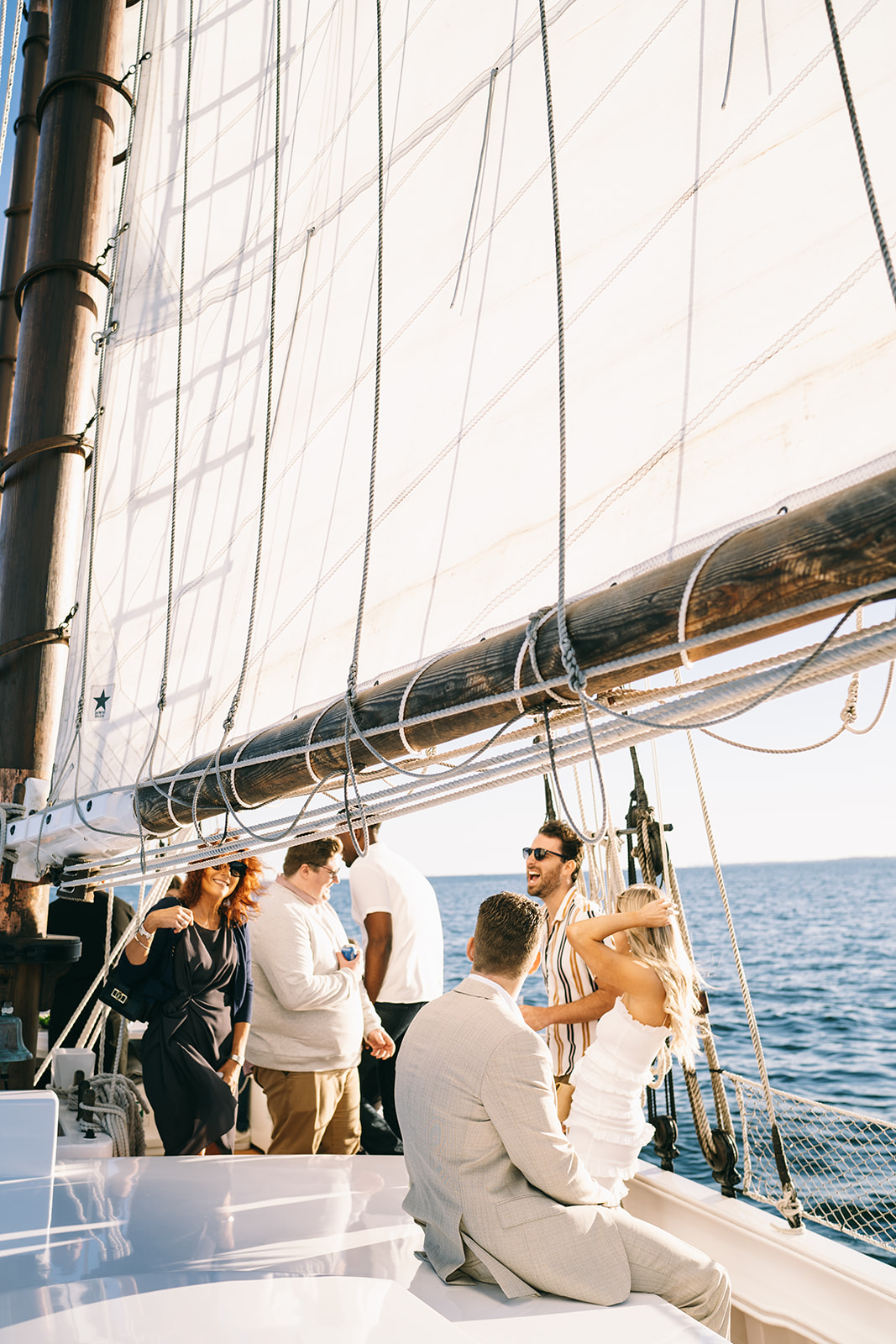 People hanging out on a sailboat on open water with the sail hoisted