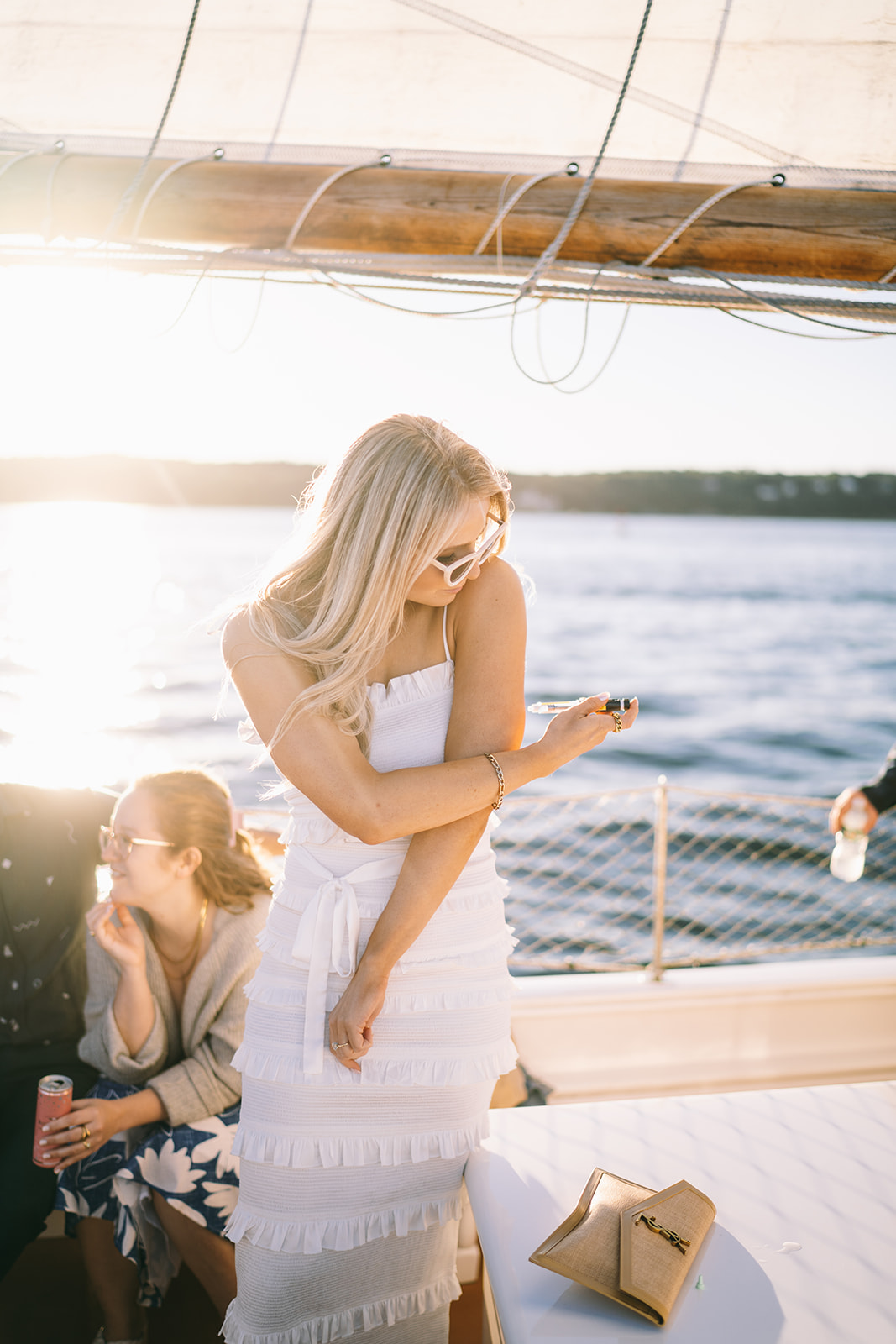 Woman in white dress on sailboat looks down at arm while giving herself insulin shot