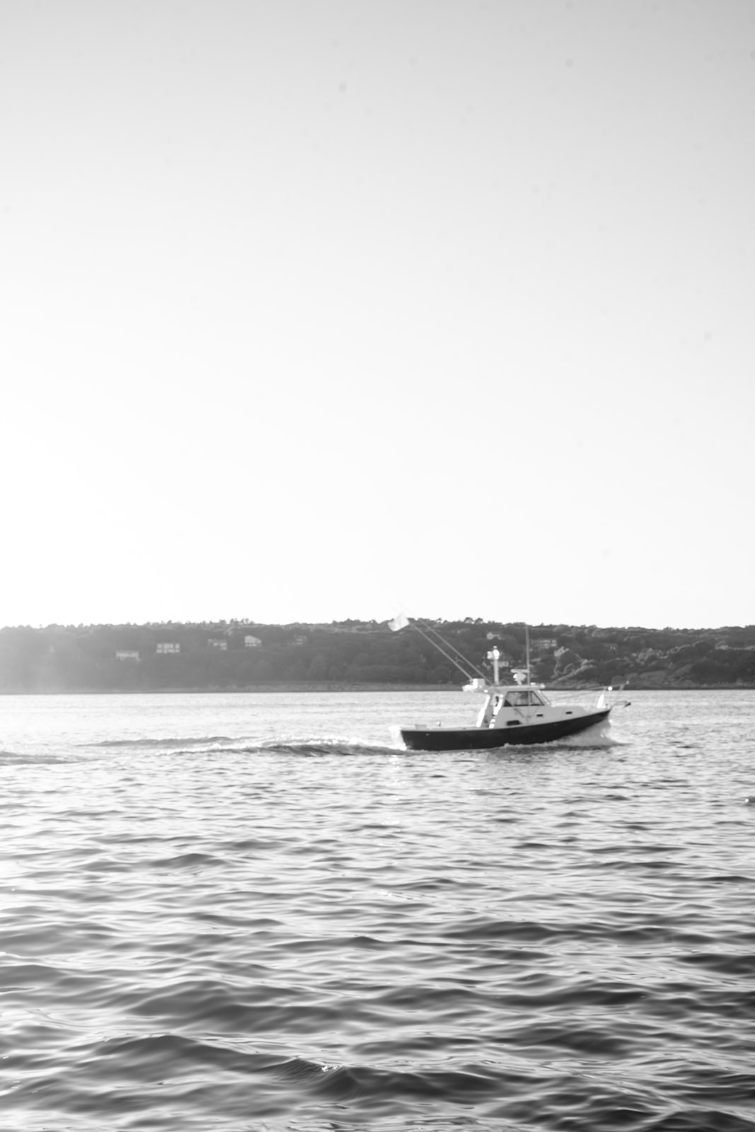 Boat sailing away on open water with small waves and forest in the background