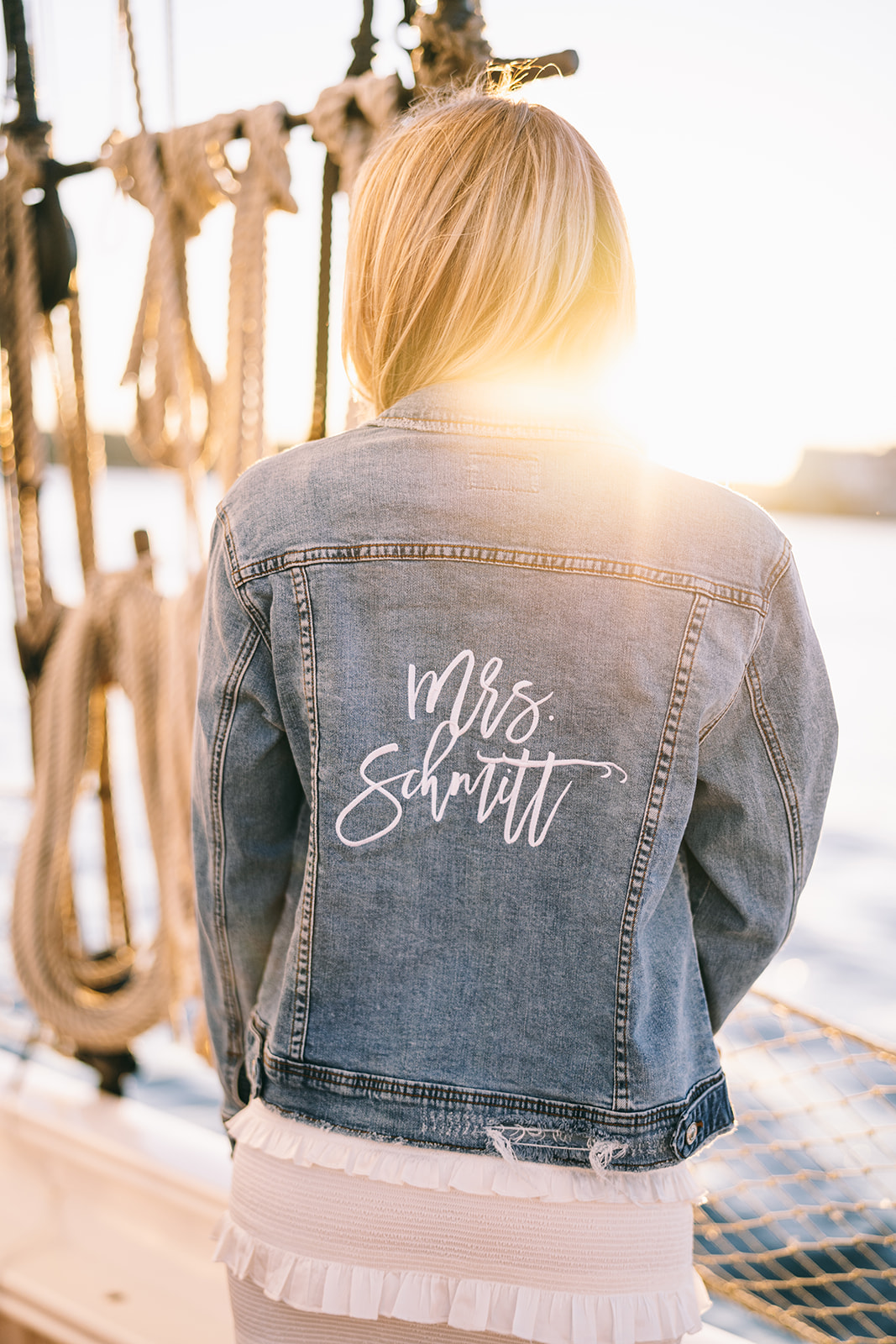 Woman wearing jean jacket that says 'Mrs. Schmitt' while the sun sets on welcome dinner sail