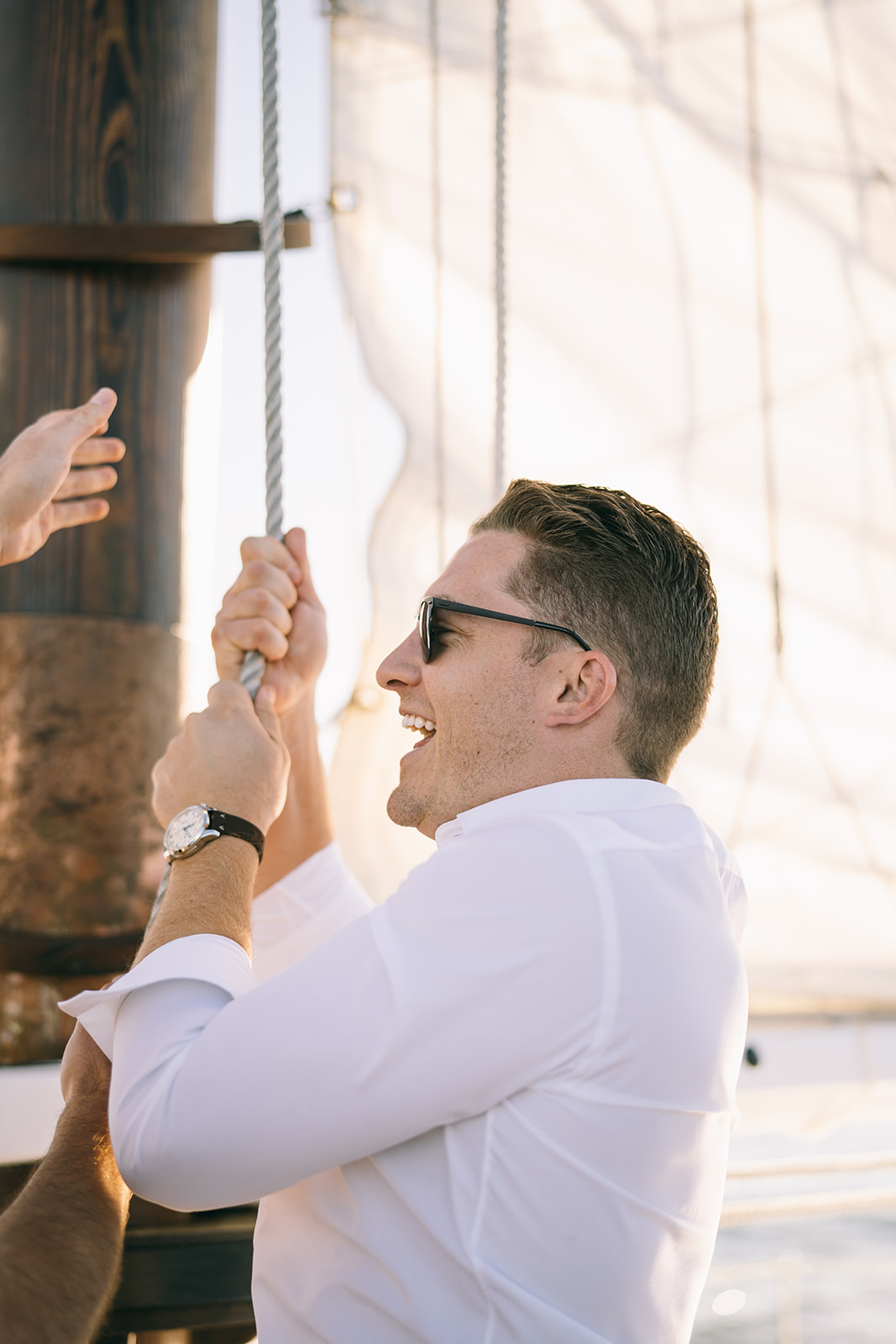 Man in white shirt and sunglasses on a sailboat pulling ropes