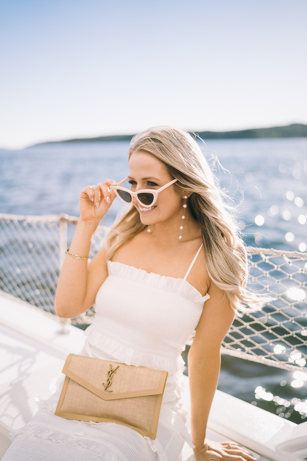 Girl sitting on side of a boat lowering her white heart shaped sunglasses smiling