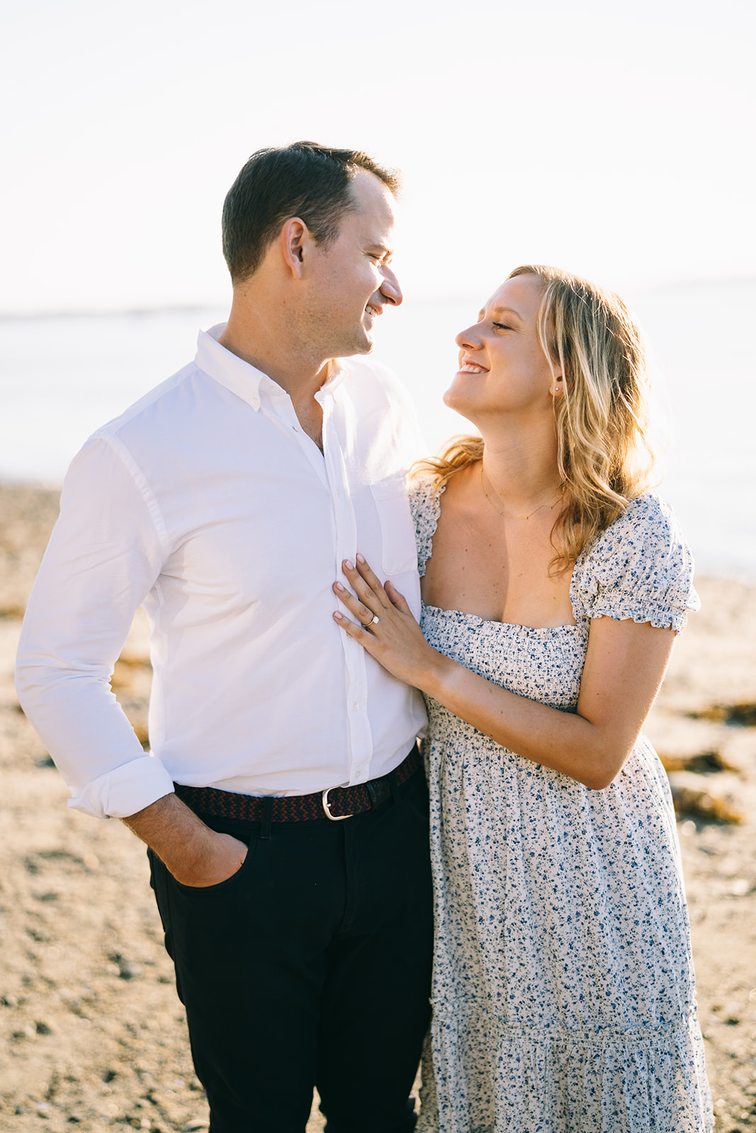 Woman in a blue and white flowered dress standing next to a man in a white shirt and blue slacks and she's touching his chest
