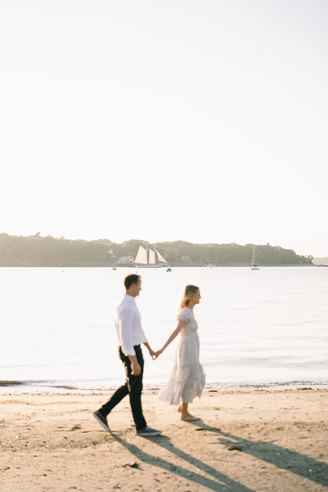 Side profile of couple walking along the sand with the ocean behind them and a sailboat in the water