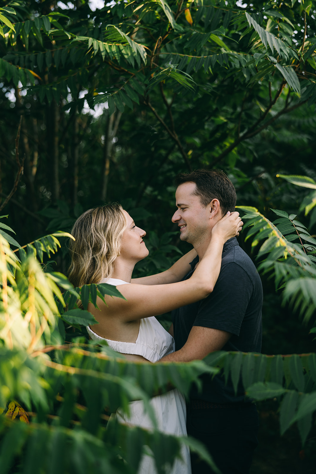 Surrounded by tropical trees, a man puts his arms around a woman's waist and she has her hands resting on his shoulder
