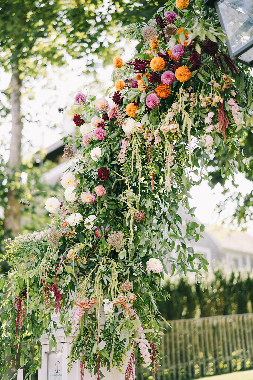 Flower arch with lots of greenery and pink, orange, and red flowers