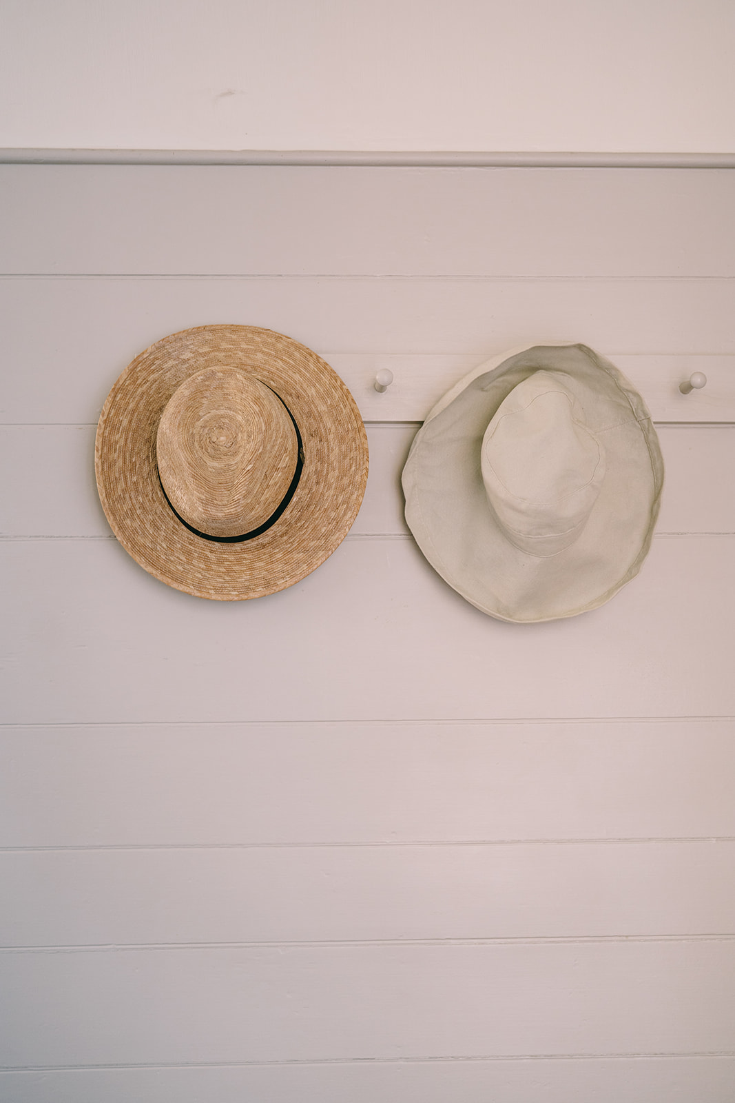 One wicker hat and one white hat hanging on hat rack
