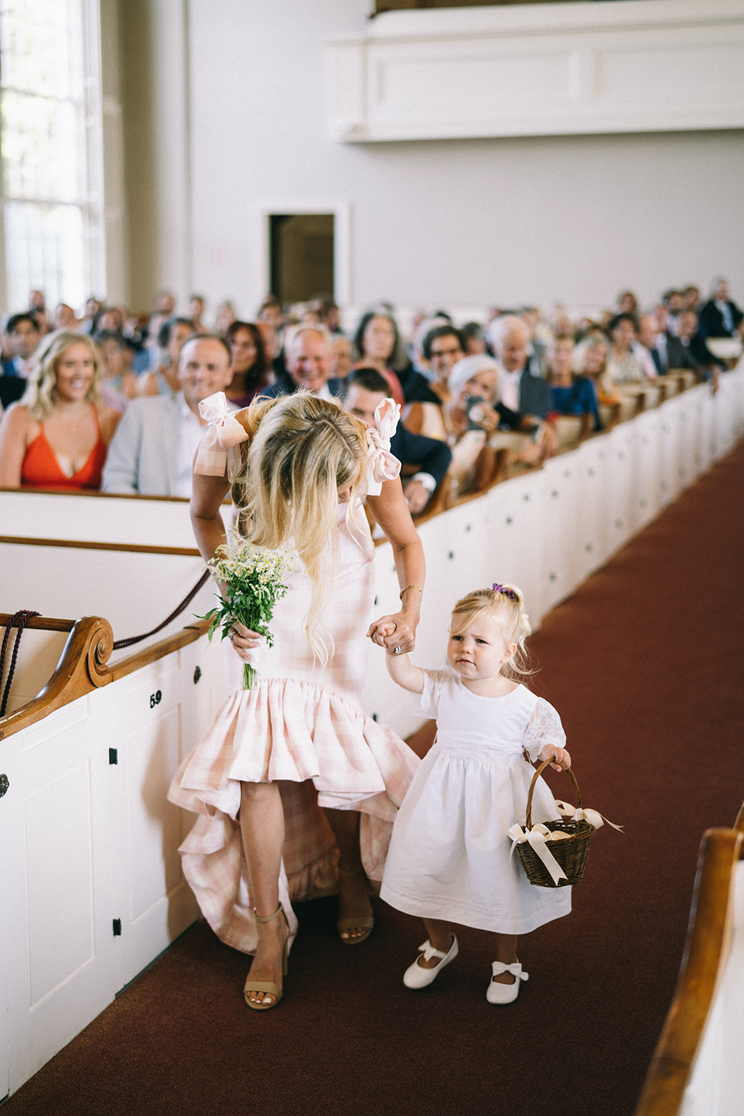 Woman in white and pink checkered dress walking down the aisle with little flower girl