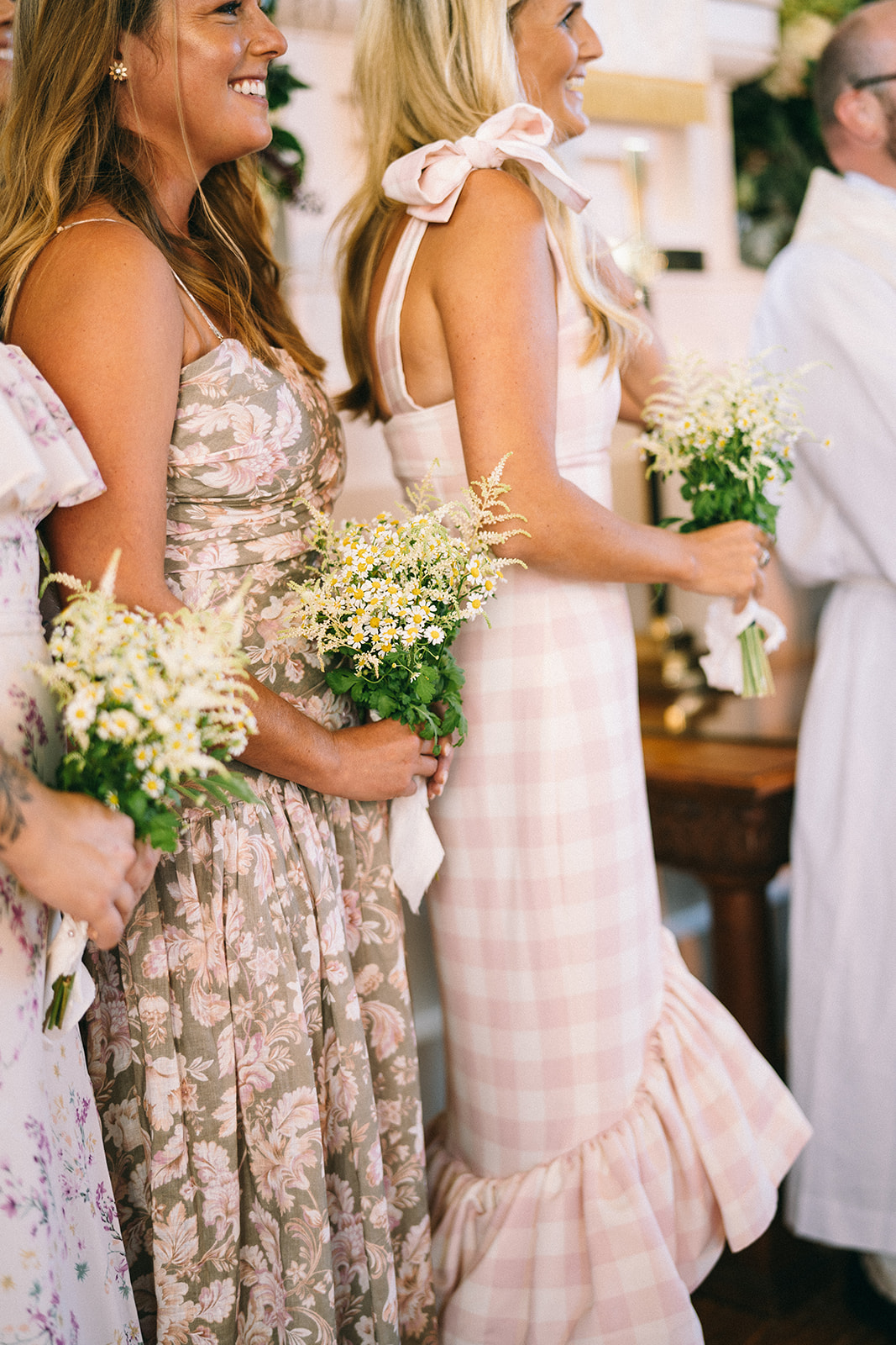 Women in pink flowery dresses holding small off white flower bouquets standing together and smiling