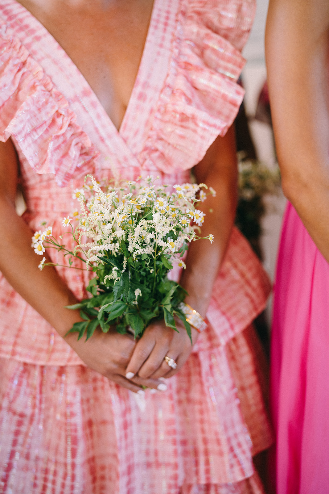 Women in bright pink and white checkered dres holding off white flowers 