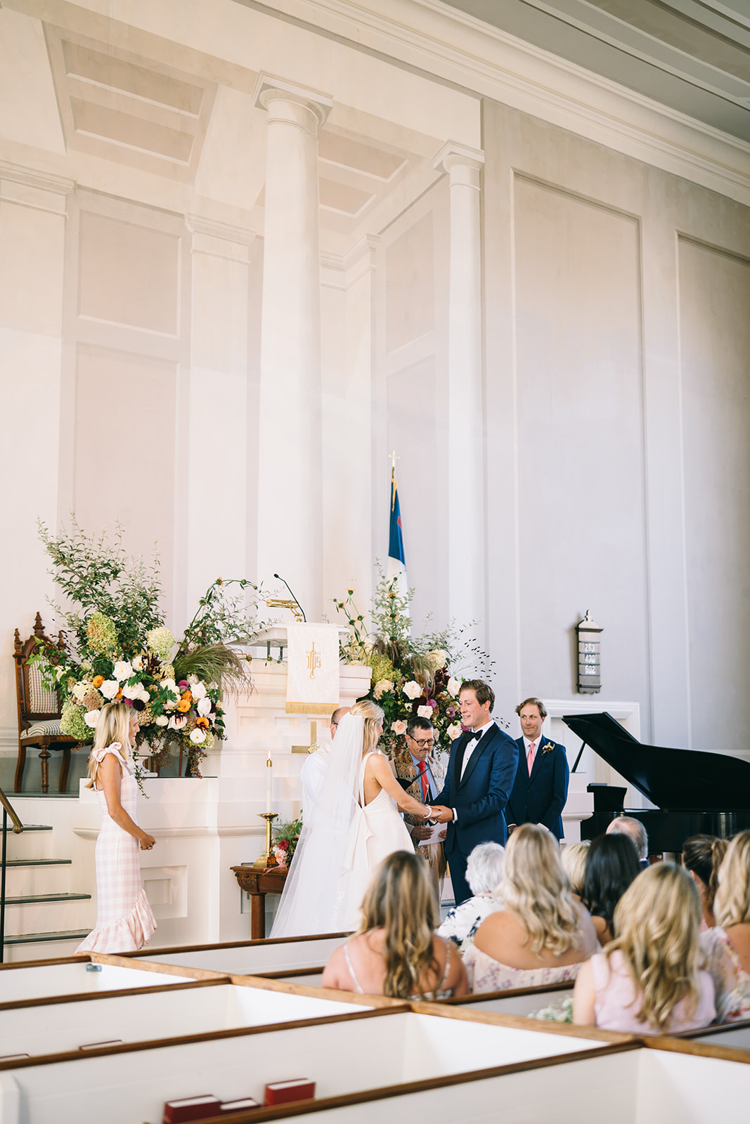 Bride and groom at the front of the church holding hands while guests watch