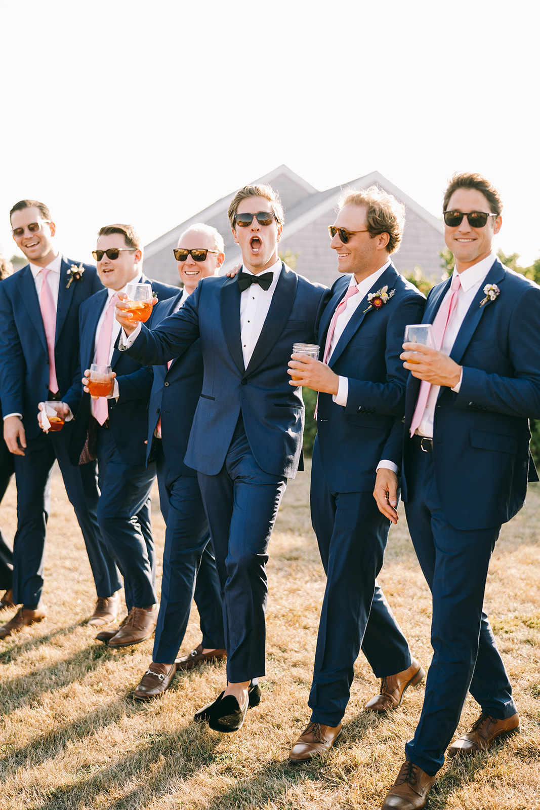 Groomsmen of wedding party walking together being excited and holding drinks 