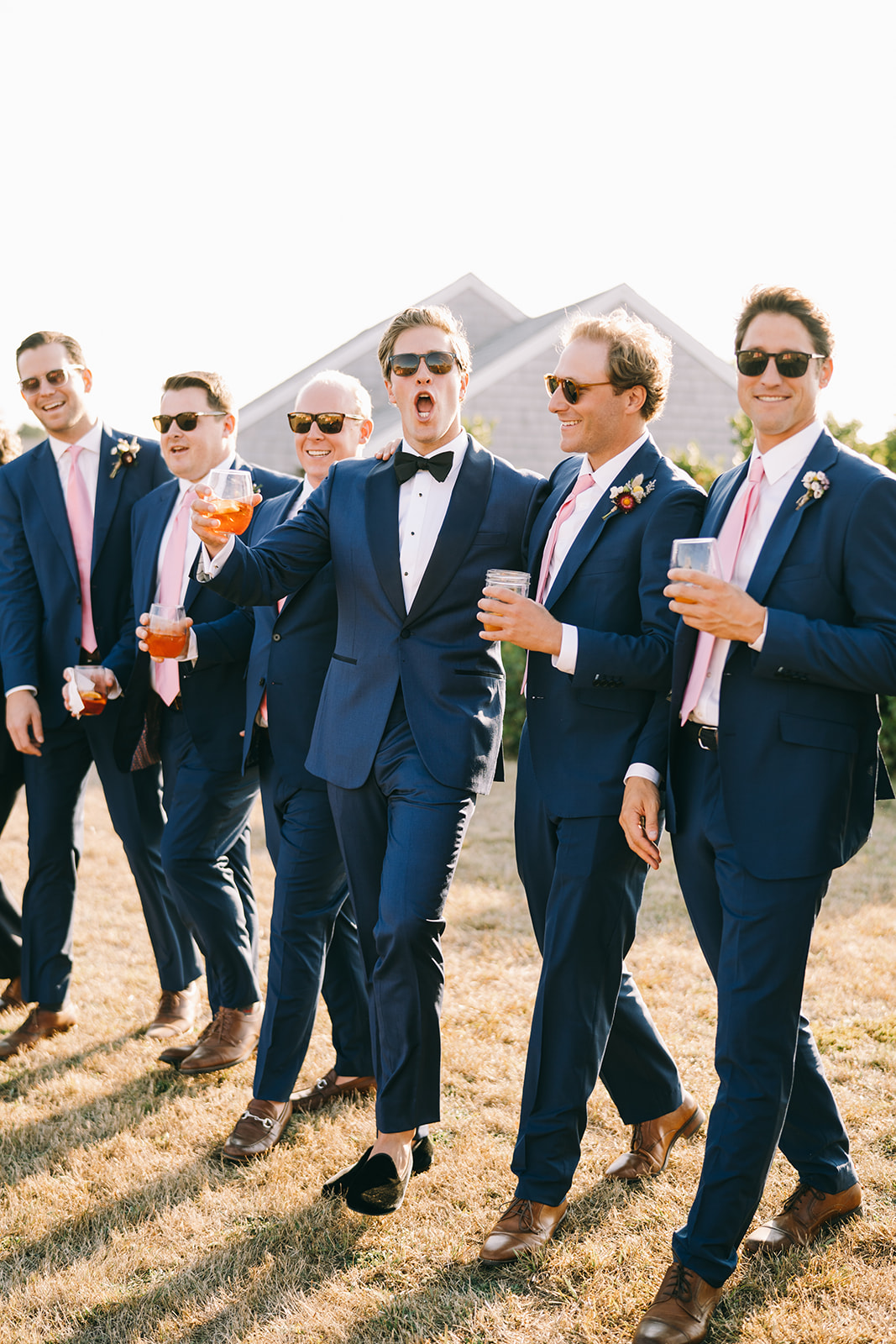 Groomsmen of wedding party walking together being excited and holding drinks 