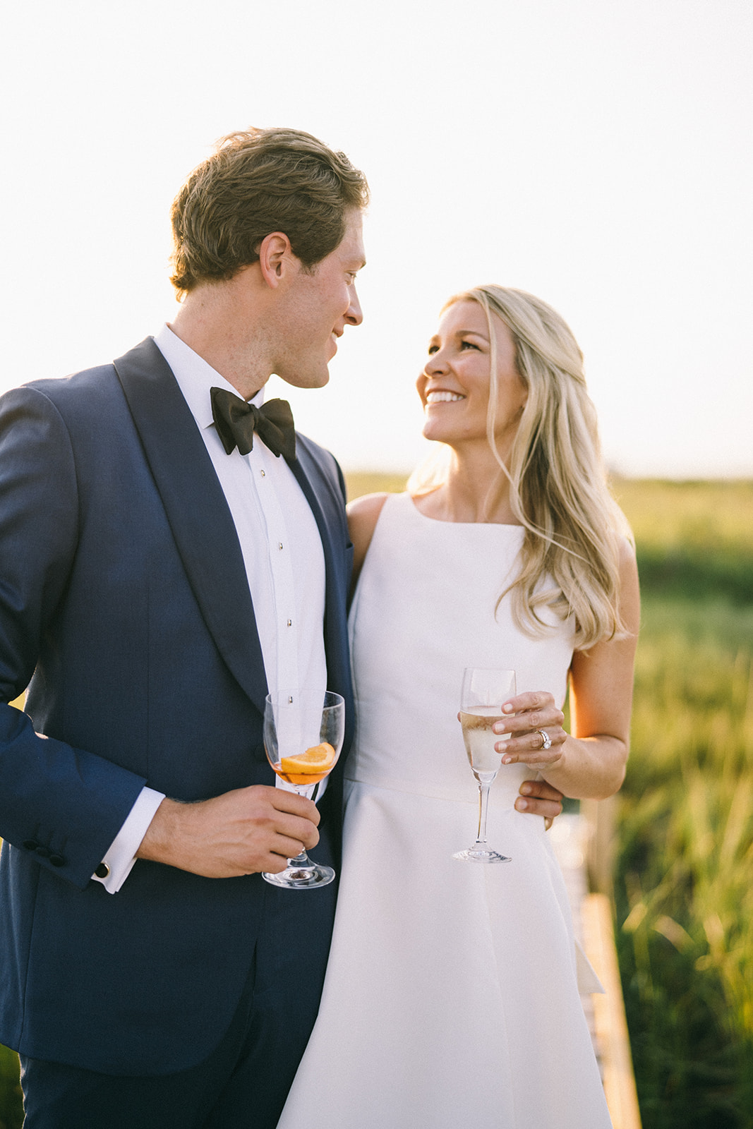 Bride and groom looking at each other and smiling while holding cocktails 