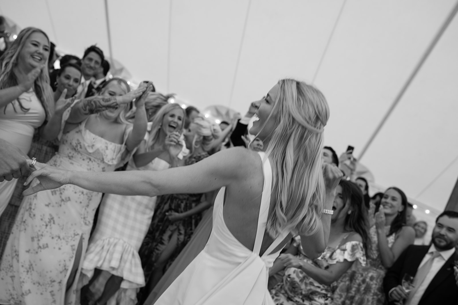 Bride laughing and pointing to guests watching her dance on the dance floor 