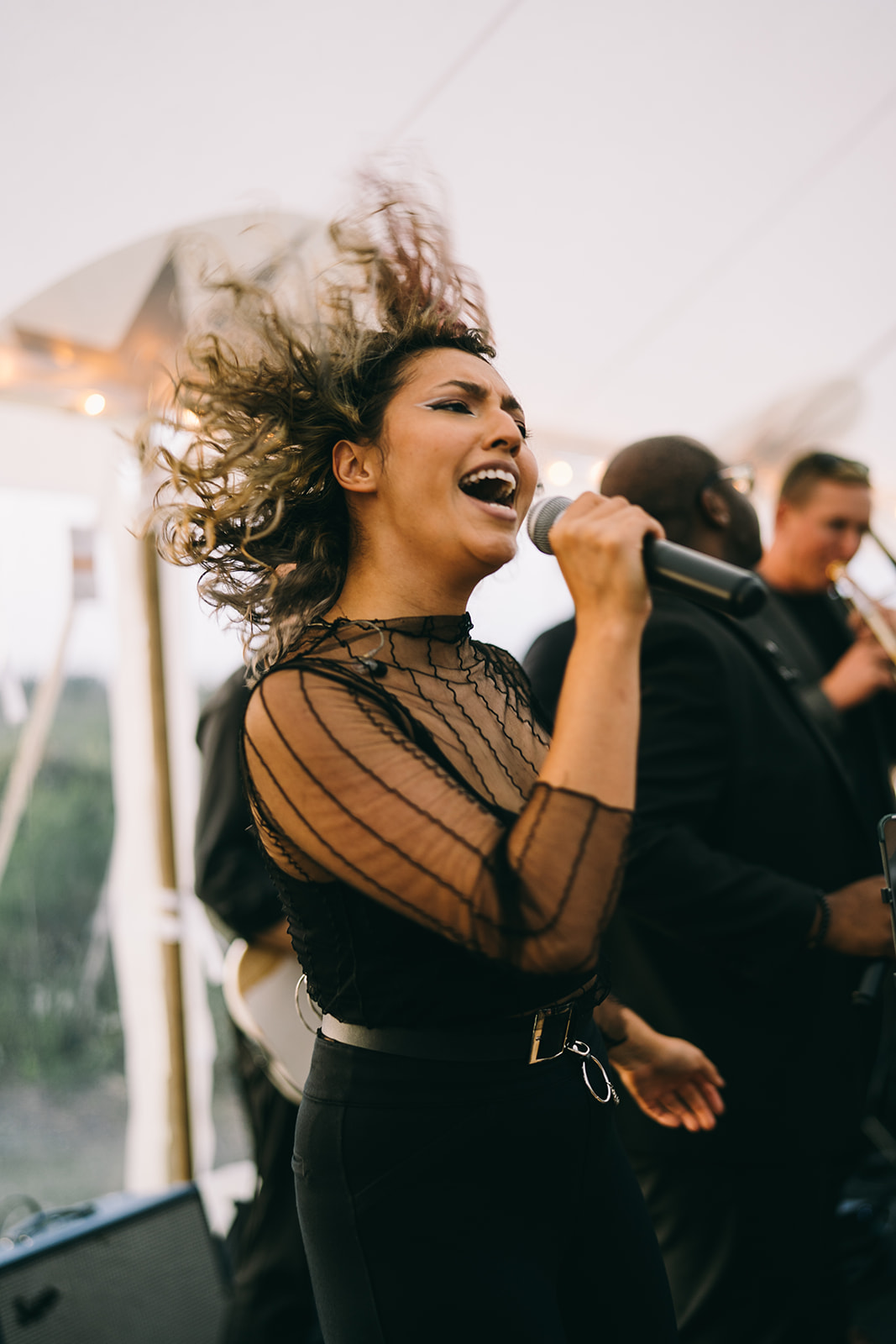 Woman in black holding a microphone and singing with her hair flying every direction 