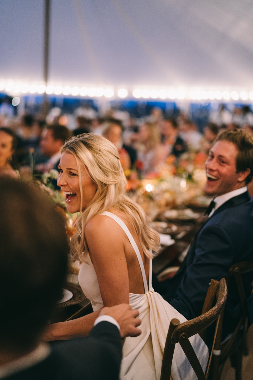 Bride laughing at wedding table while looking out on her guests 
