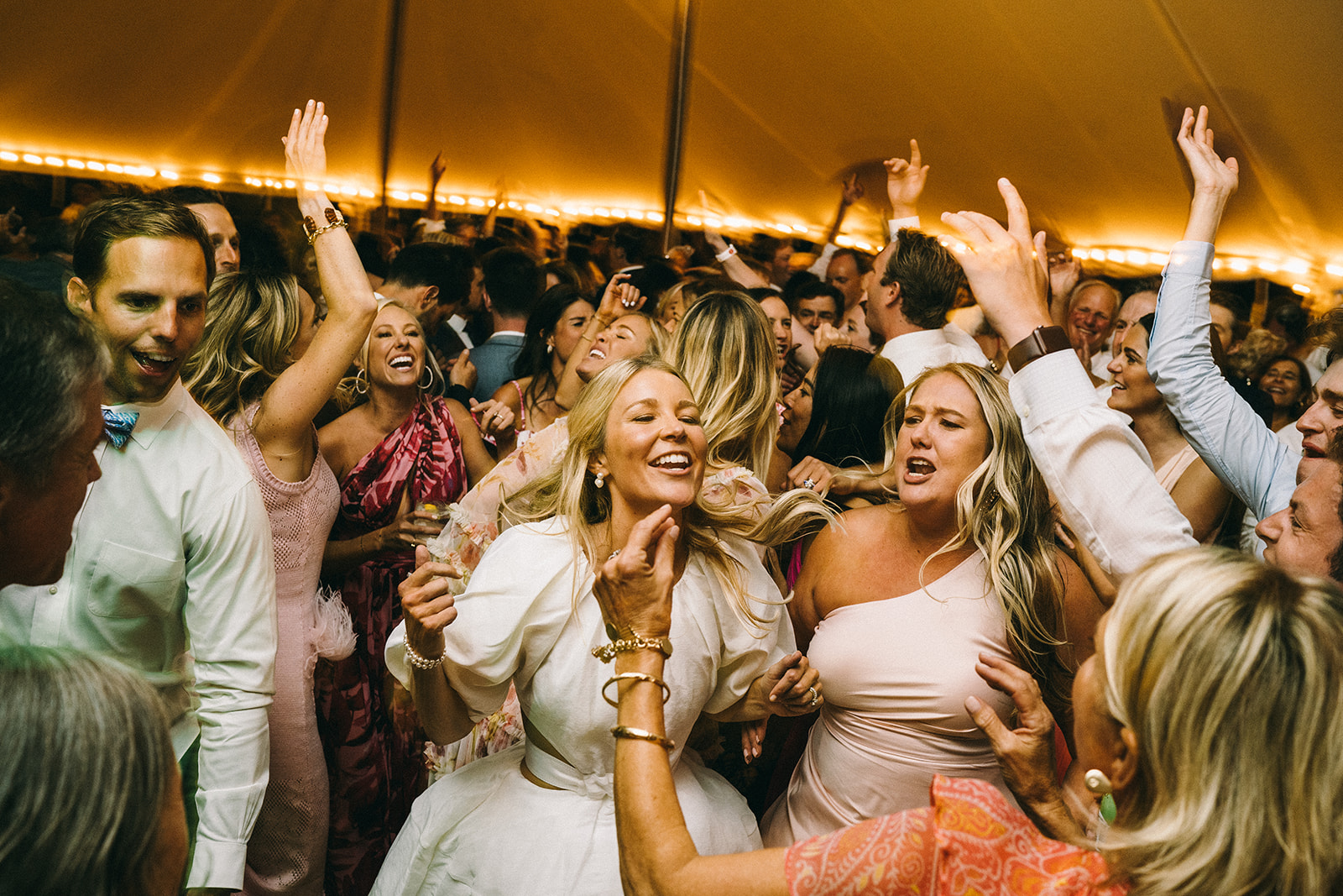 Wedding reception with the dance floor completely full and two women in the foreground with blonde hair smiling and jumping 
