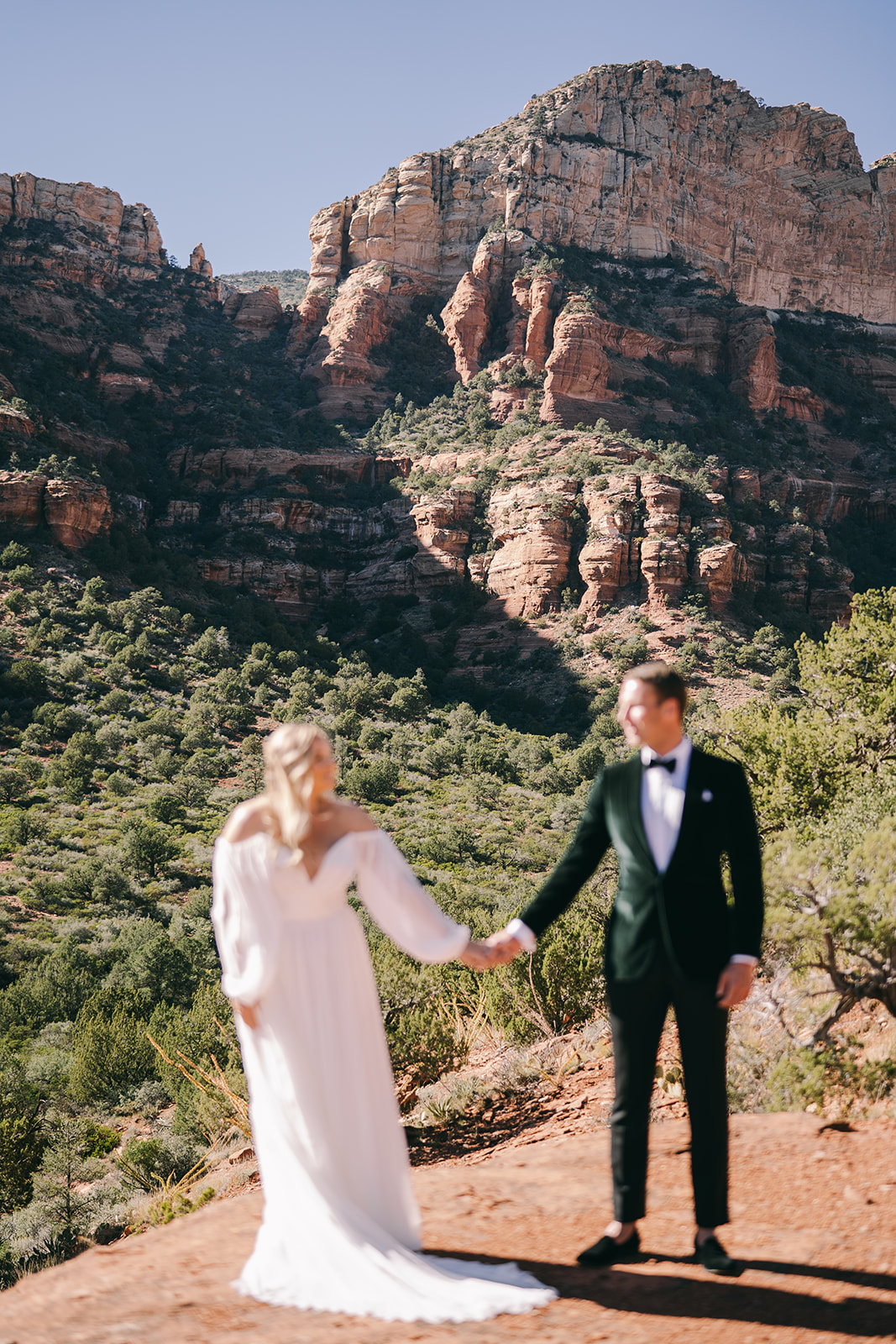 Bride and groom standing in front of mountain in Sedona out of focus with the mountains in focus 