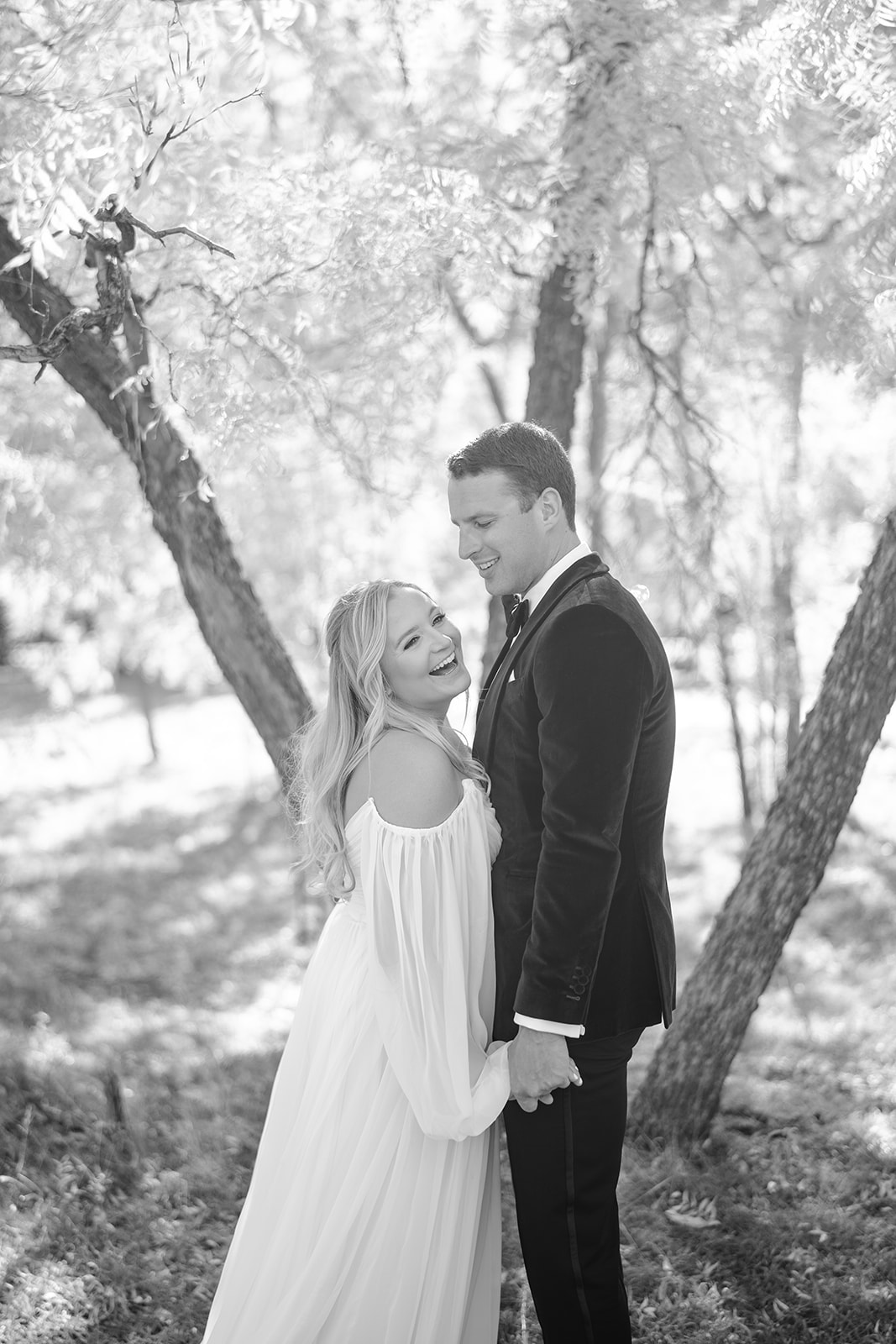 Bride and groom standing chest to chest laughing with trees and soft light in the background 