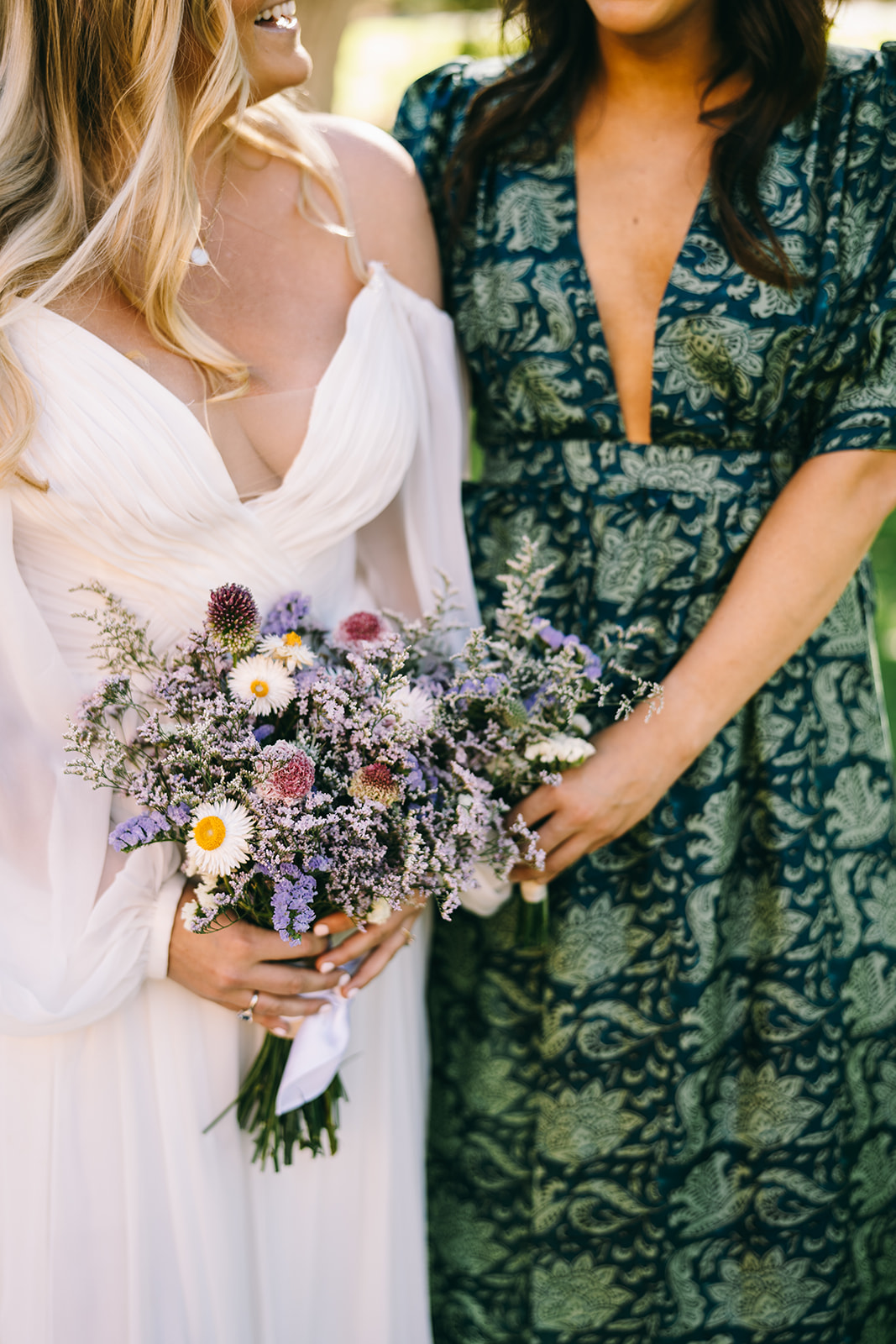Bride holding purple and white flowers standing next eo a woman in green and blue dress