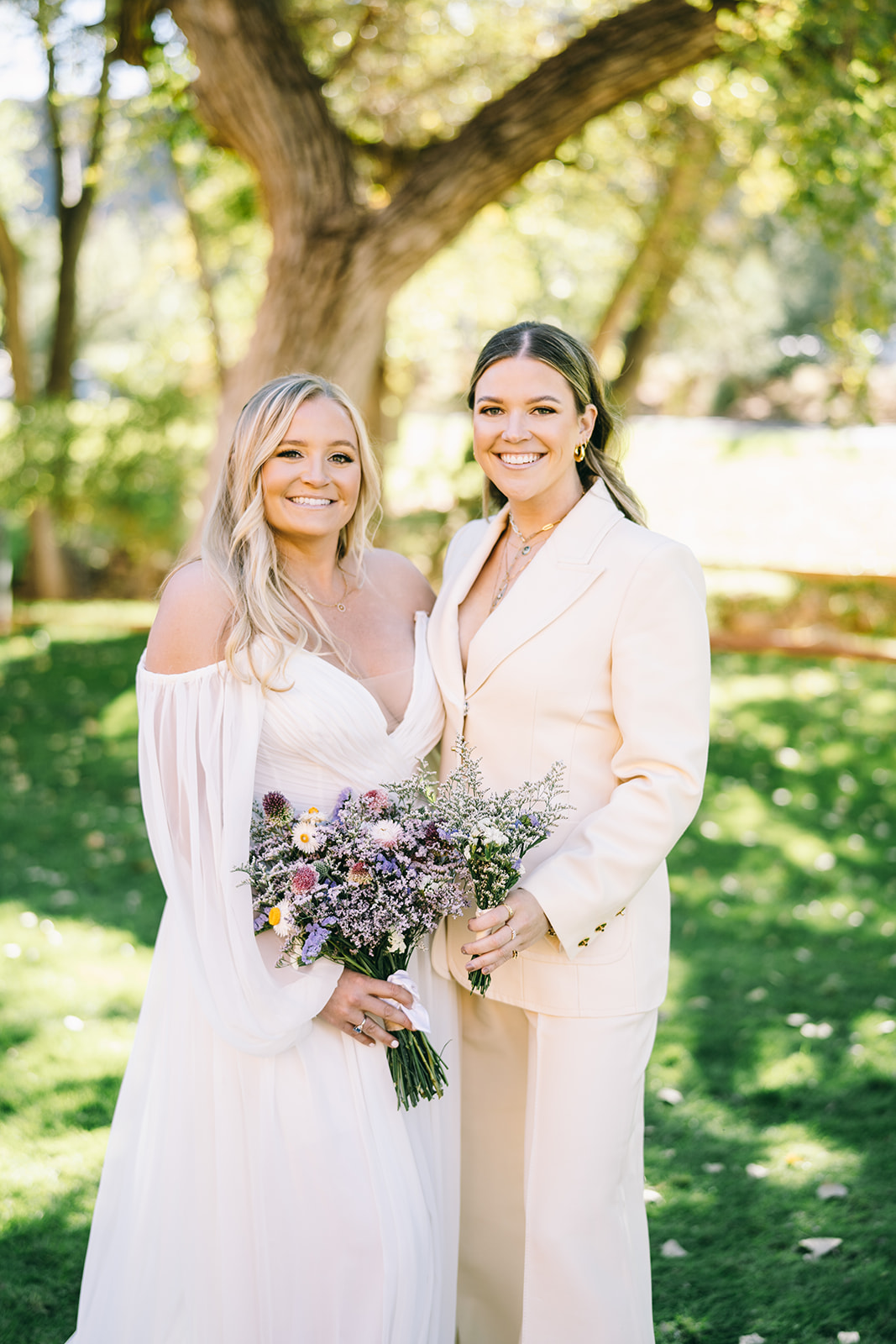 Bride standing with bouquet next to a woman in a beige outfit