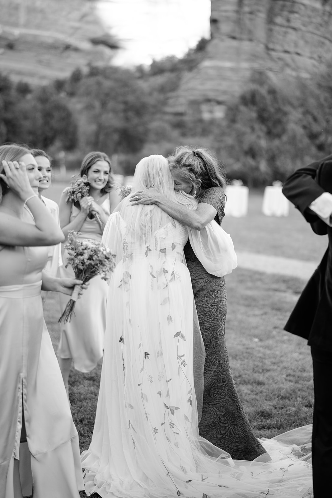 Bride with flower petals in her veil and woman hugging in black and white 