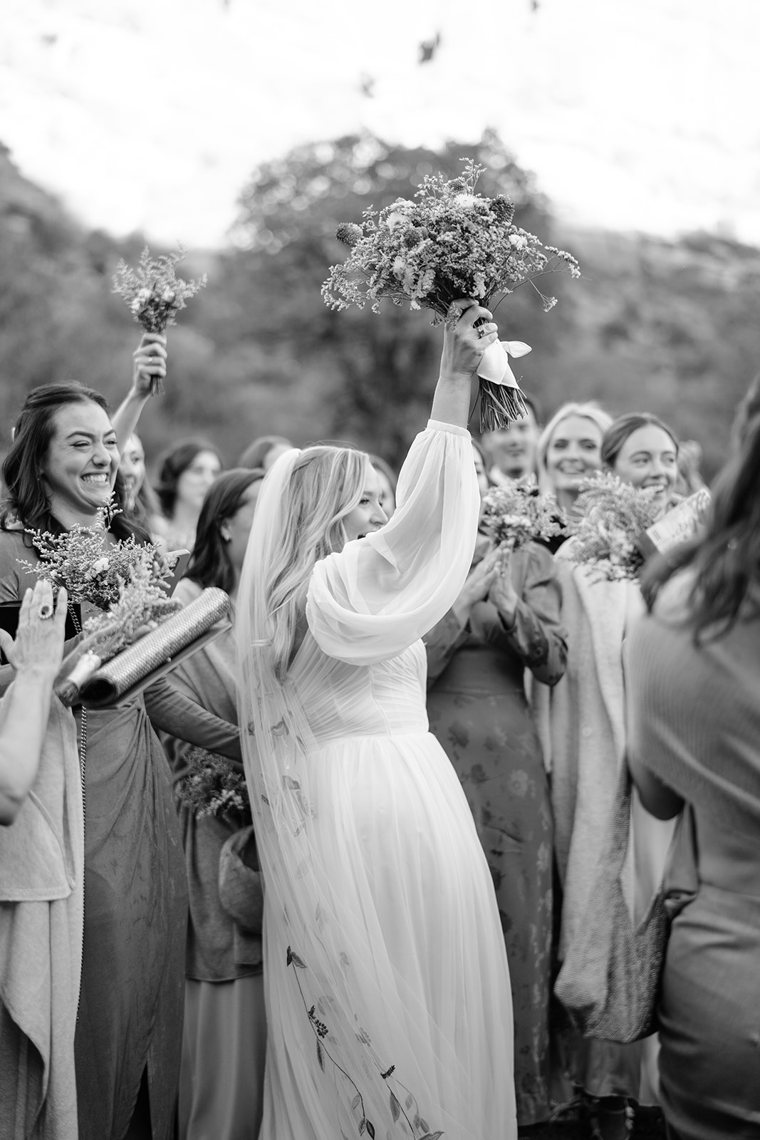 Bride and bridal party smiling with the bride holding up her flowers in the air 