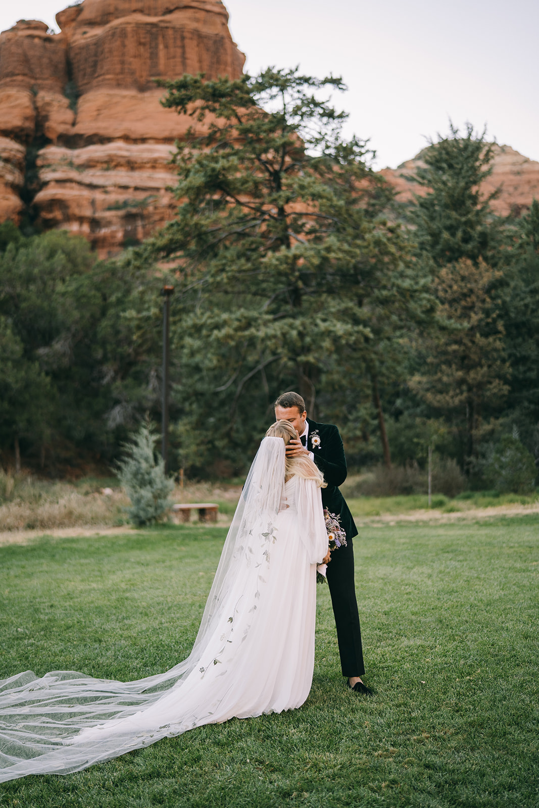 Groom kissing the bride with Sedona mountains in background with the bridal veil flowing