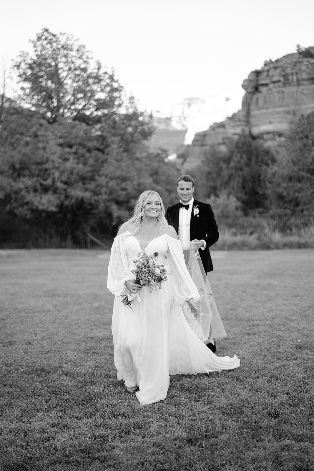 Groom holding brides veil as he follows her 