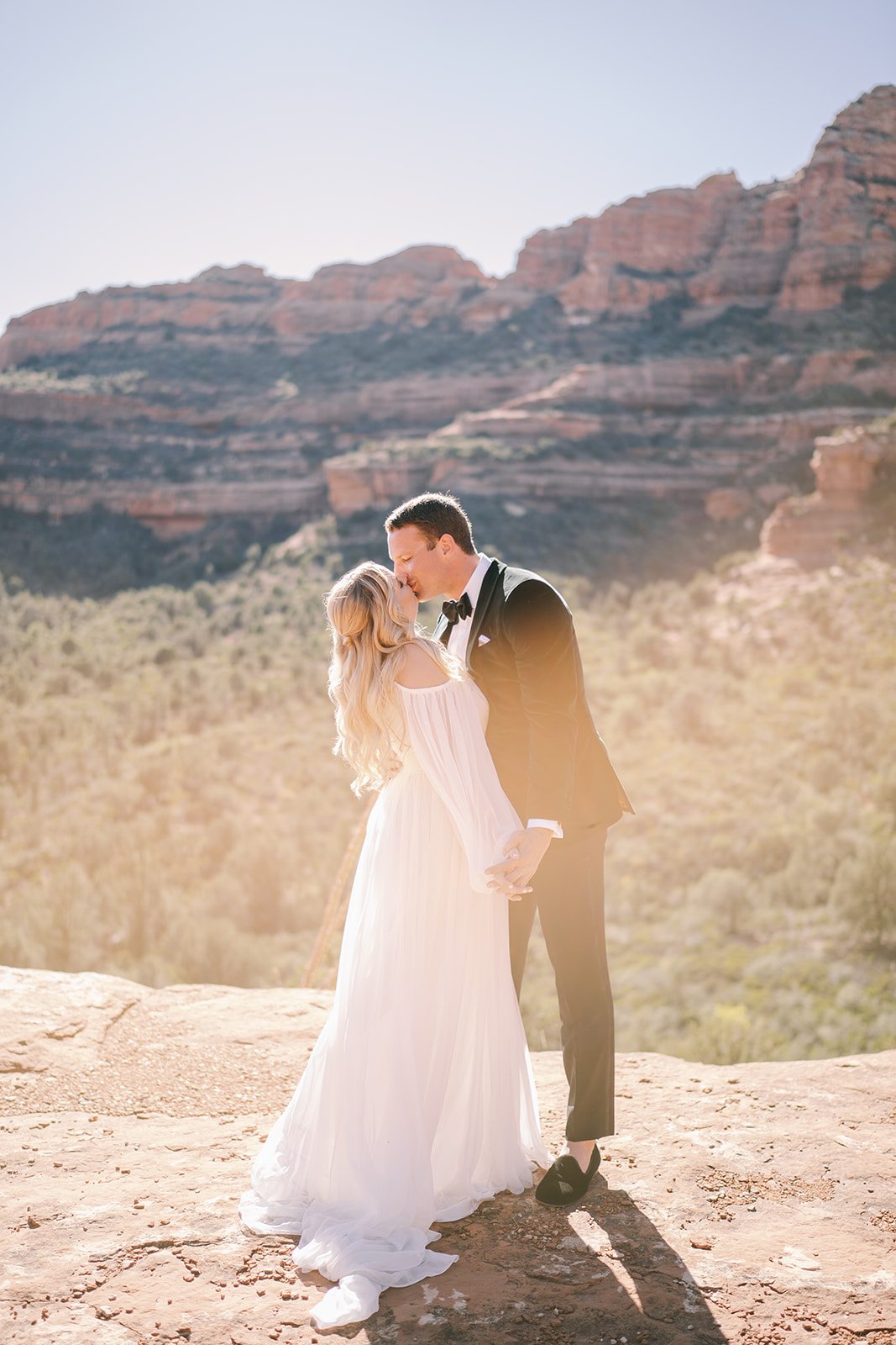 Bride and groom kissing with Sedona mountains in background with soft light 