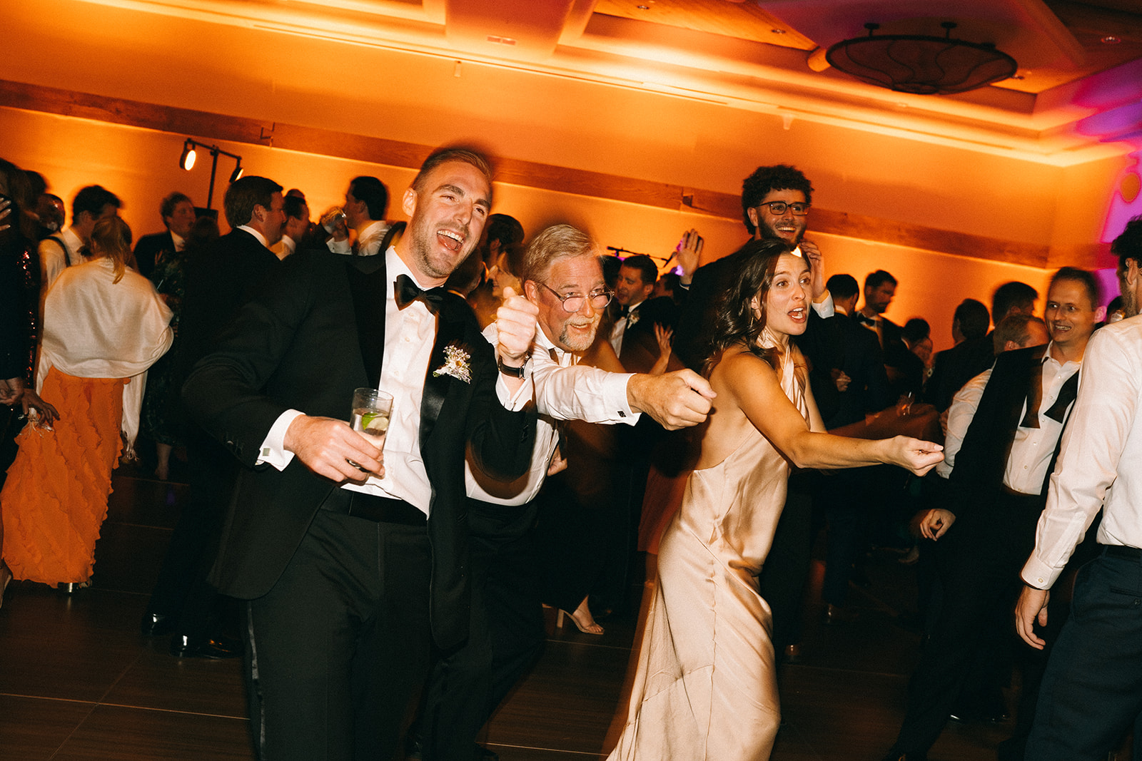 Two men laughing and pointing and a woman in gold dress making a pulling motion and laughing 