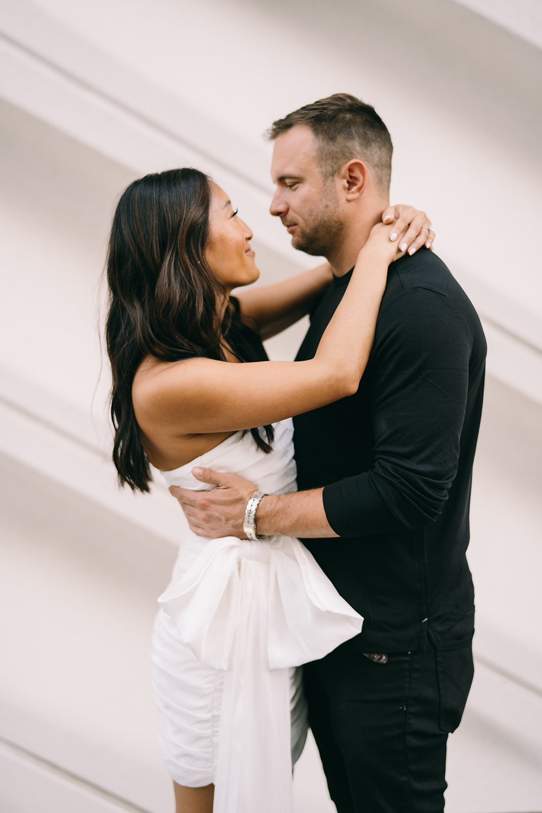 zoomed in woman smiling in short strapless white dress with her arms around a man in black 