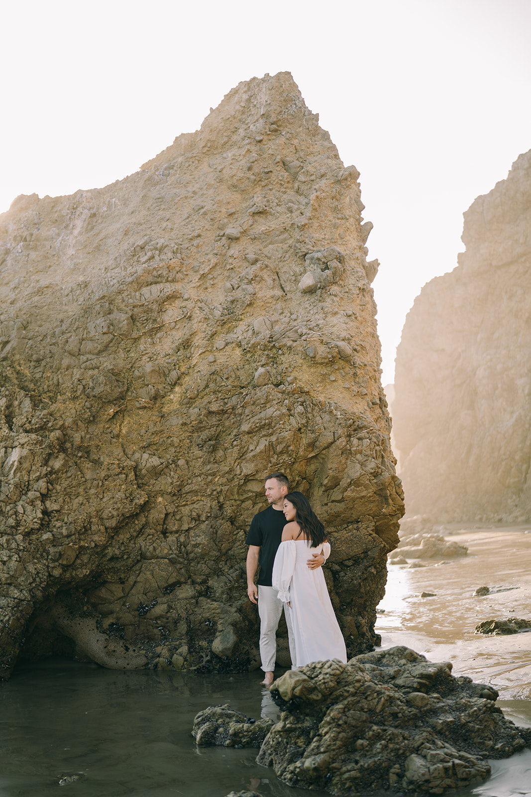 Couple in front of a large rock on the coastline embracing