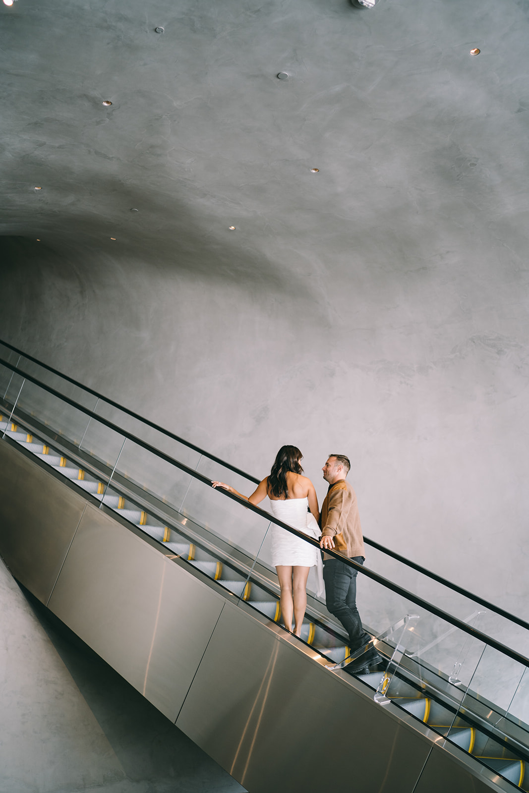 Couple going up an escalator in a light gray tunnel