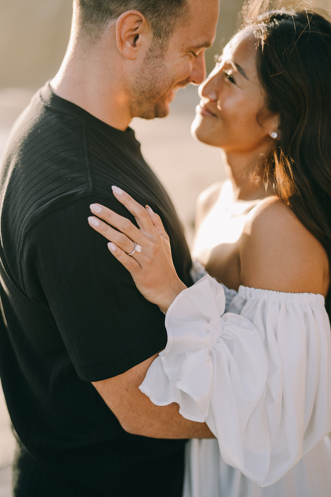 Close up of couple smiling with woman's hand on man's shoulder displaying large engagement ring 