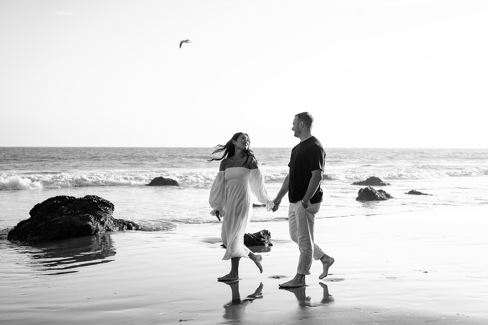 Couple on the beach with waves crashing behind them and a clear sky above malibu engagement el matador beach california