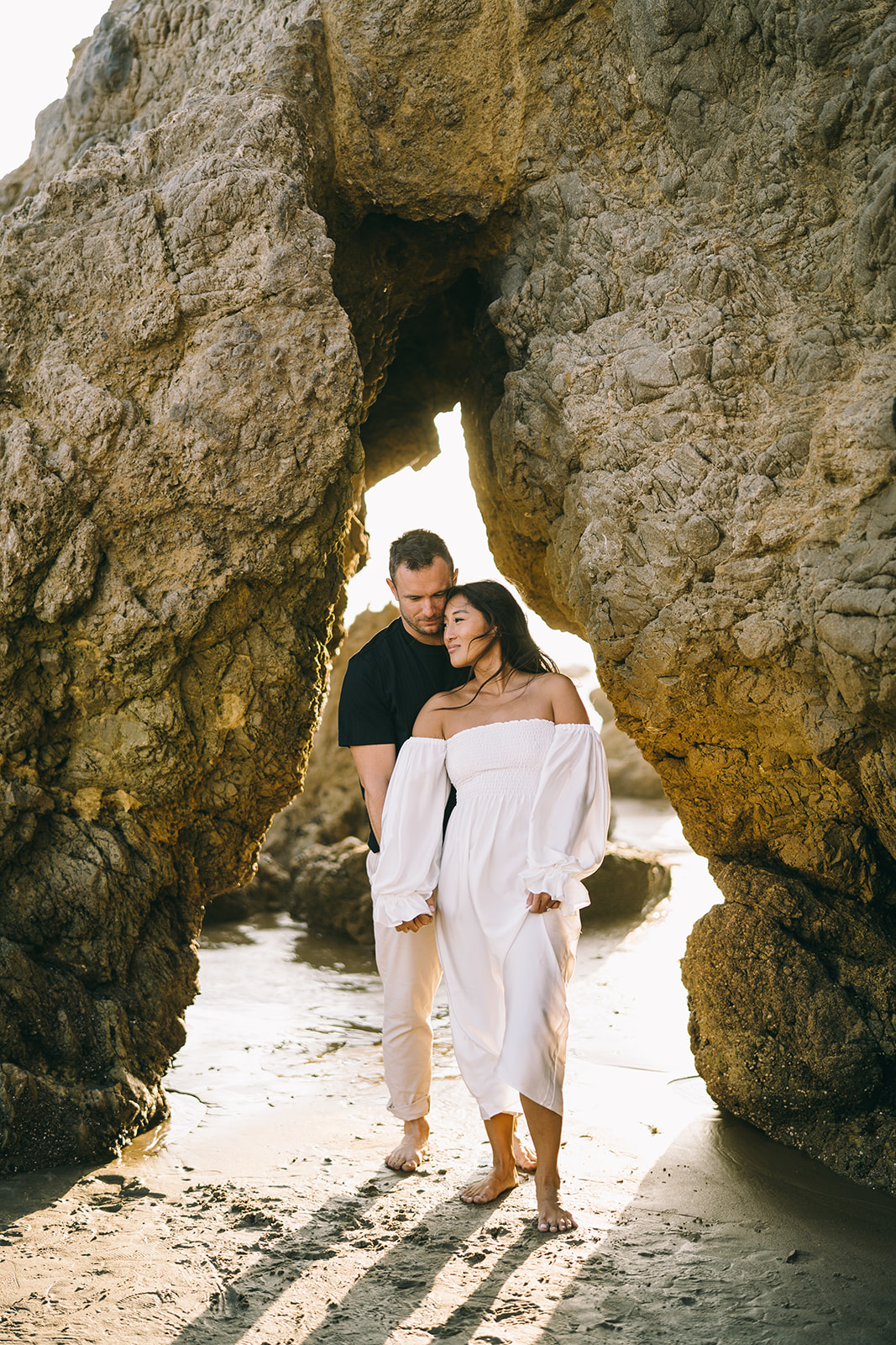 Man and woman standing close together in a rock arch on Malibu beach